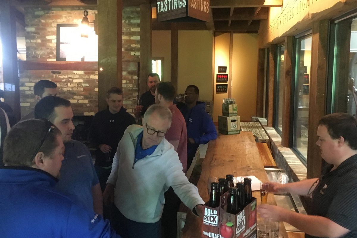 Riders crowding a cider tasting bar, Bold Rock six-packs on the counter