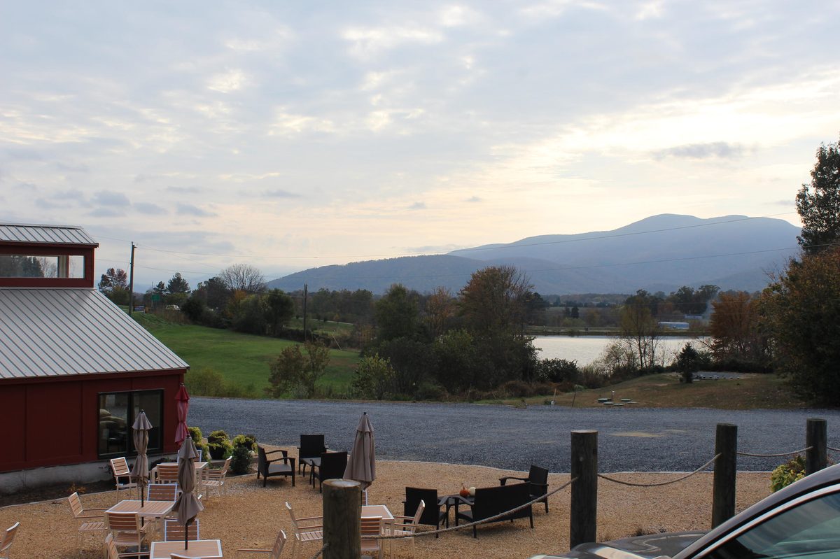 A red tasting-room corner and a gravel patio overlooking a pond and a mountain at golden hour